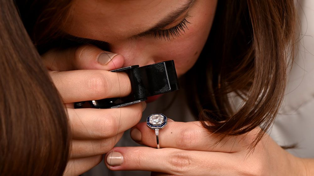 13025 Customer using a Loupe on a Diamond and Sapphire Halo Engagement Ring in Showroom